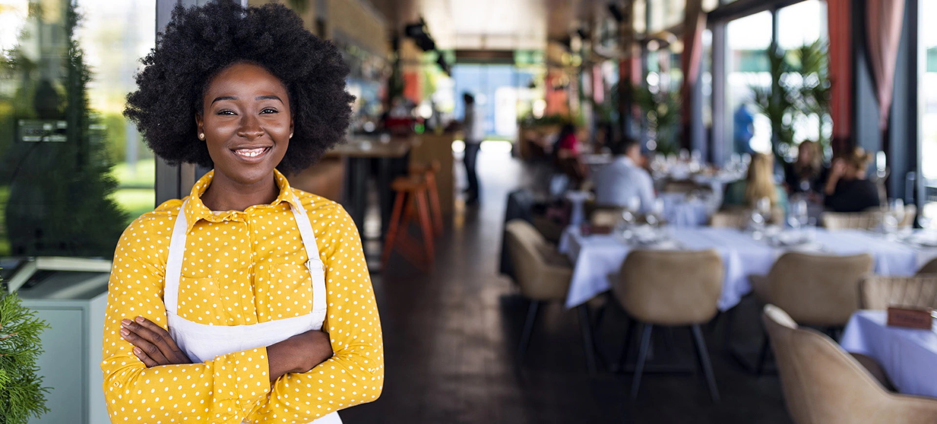 Female restaurant worker standing outside of a restaurant with her arms crossed and smiling