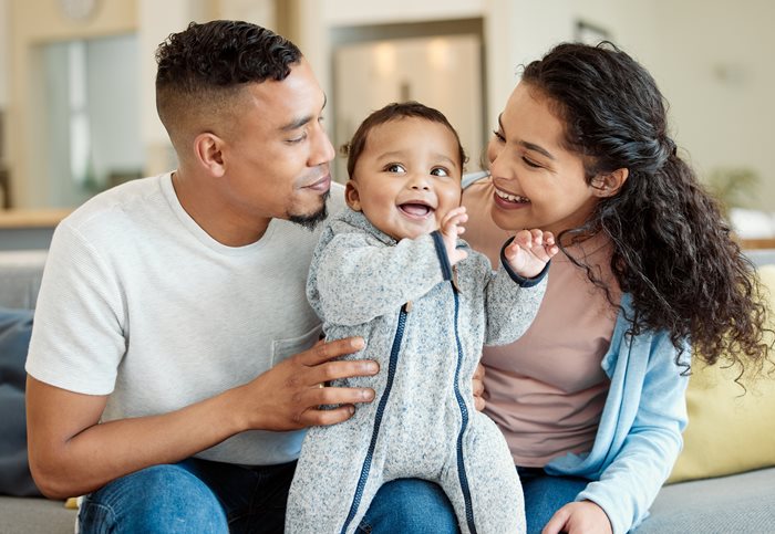 A family sitting on the couch, with the man and woman looking at their baby and smiling