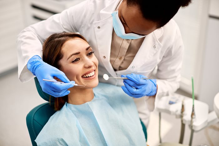 A woman sitting in the dentist chair smiling while the dentist stands over her checking her teeth